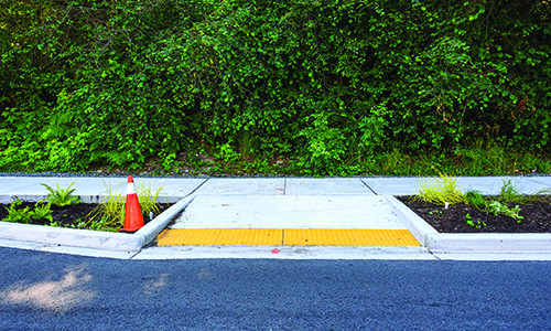 Yellow curb cut on a sidewalk with an orange safety cone