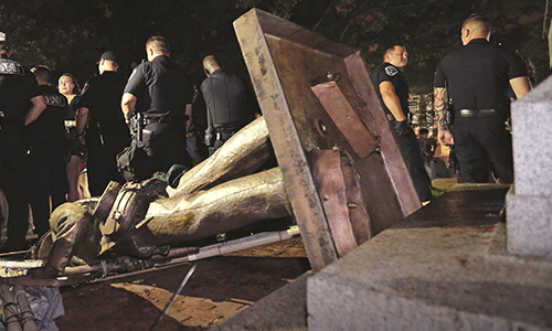 Police officers stand next to a toppled confederatesoldier statue.