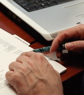Closeup of a hand holding a pen near paper and a laptop