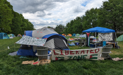 Encampment shows tents arranged in a rectangle on a lawn with banners declaring "Liberated Zone" and "People's College for the Liberation of Palestine"