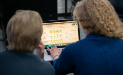 Two people viewed from the back look on at a computer screen with a financial spreadsheet