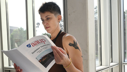 Person in front of a large window flips through an AAUP Summer Institute program.