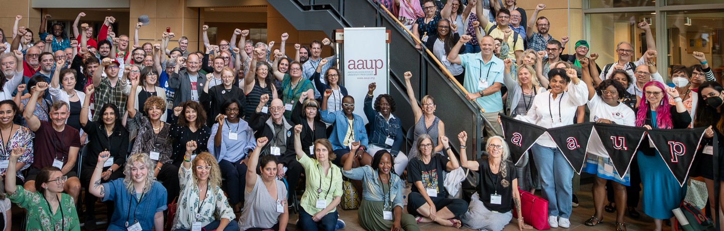 Large group of AAUP members stand with fists raised on and next to a stairway, with many of them holding AAUP signs